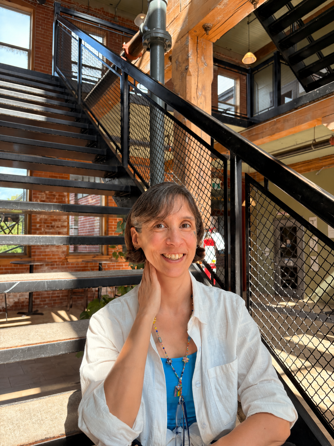 Headshot of Arria, smiling, sitting on a stairs in an industrial loft setting.